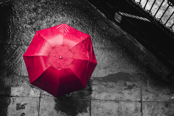 black and white rain puddle on sidewalk, top view of red umbrella